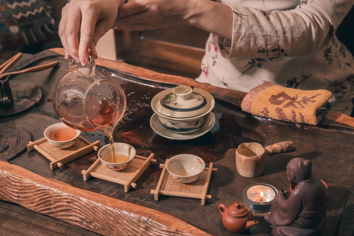 A traditional tea ceremony in progress, with tea being poured into small cups on a wooden table.