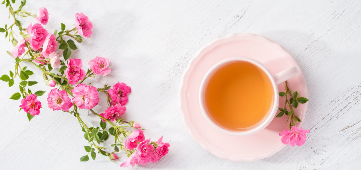Pink roses next to a cup of tea on a pink saucer.