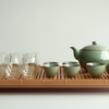 Bamboo tea tray with a green ceramic teapot set, four matching teacups, and multiple double-walled glass cups arranged neatly for tea service.