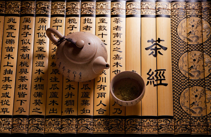 An ornate bamboo scroll featuring elegant calligraphy and symbols, accompanied by a traditional clay teapot and a cup filled with green tea, highlighting the cultural essence of tea and its ancient heritage.