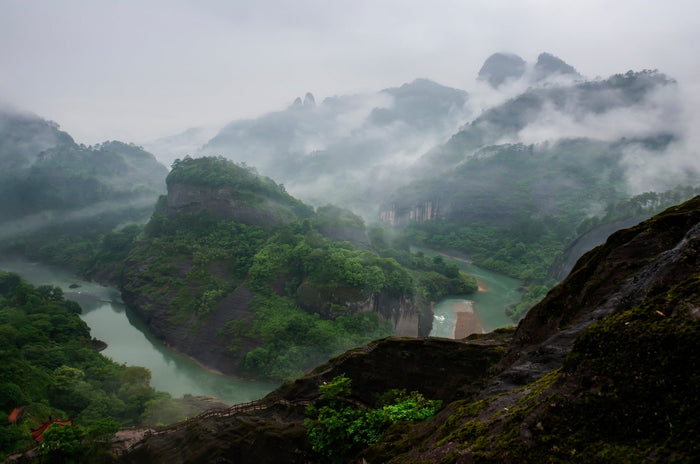 A breathtaking view of Wuyi Mountain in Fujian, China, covered in mist with lush green peaks and winding rivers, showcasing the iconic landscape where famous Fujian oolong tea is grown.