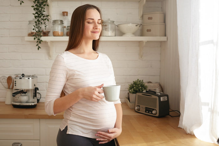 A pregnant woman in a cozy kitchen enjoying a warm cup of tea, smiling peacefully while holding her belly, symbolizing relaxation and mindful pregnancy nutrition.