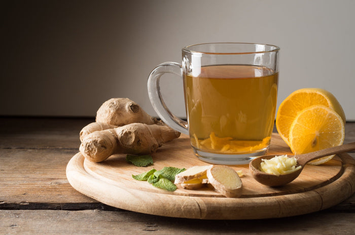 A warm cup of ginger tea infused with fresh ginger slices, lemon, and mint, placed on a rustic wooden board with additional ingredients nearby, highlighting its natural health benefits.