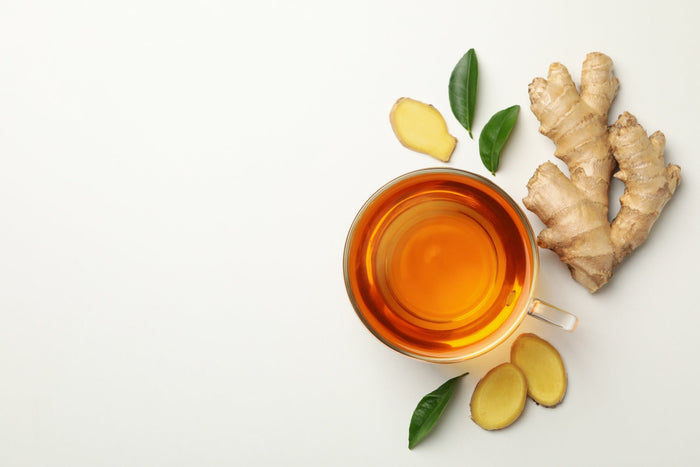 A cup of ginger tea with fresh ginger root, sliced ginger, and tea leaves on a white background. A refreshing and healthy herbal tea known for its warming and digestive benefits.