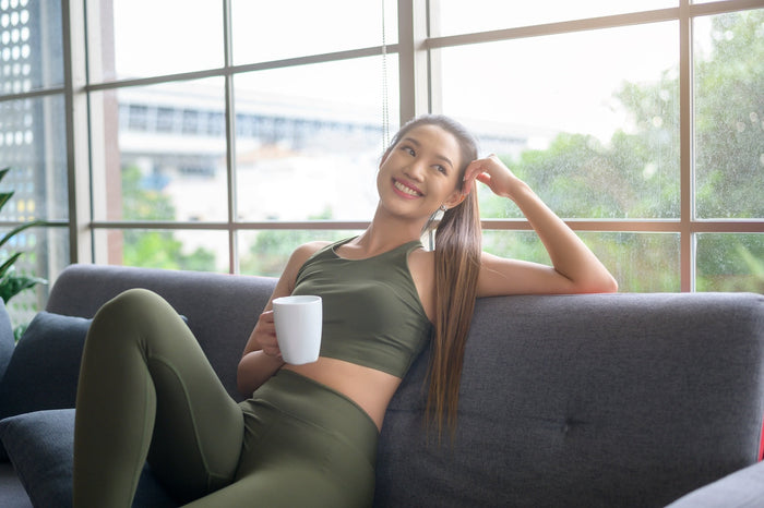 A smiling woman relaxing on a couch, enjoying a cup of tea, symbolizing the calm and healthy lifestyle benefits associated with drinking tea for weight loss.