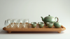 Bamboo tea tray with a green ceramic teapot set, four matching teacups, and multiple double-walled glass cups arranged neatly for tea service.