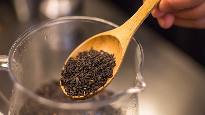 Measuring loose leaf tea with a wooden spoon over a glass teapot